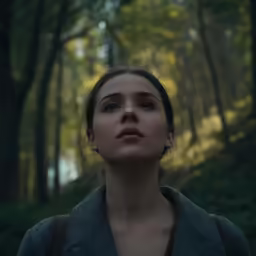 a woman wearing a brown top is standing in the forest