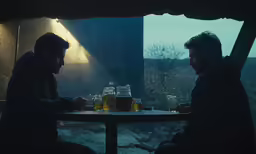 two men sitting at a table with beers