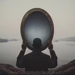 man holds an oval framed mirror on his face