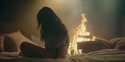 a woman sitting on the bed in front of fire