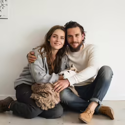 a man and woman cuddle in front of a white wall