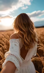 a woman standing in a wheat field at sunset