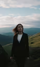 a woman walks on a dirt path near mountains