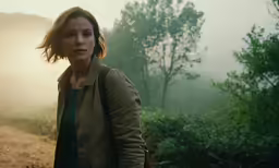 a woman standing in the woods at sunset