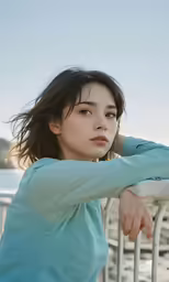 a woman in a blue shirt leaning on a fence