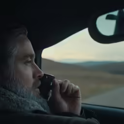 a man sits in the passenger seat of his car and talks on the phone