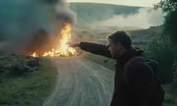 man on country road pointing at fire on asphalt