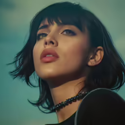a young woman with a large jeweled necklace stares up into the distance