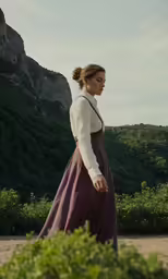 a woman wearing a purple dress stands in a field near a mountain