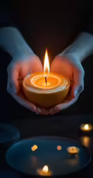 hands cupping a lit candle as it is sitting on a plate