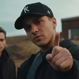 a man pointing a finger at something, the other man is wearing a baseball cap