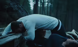 two people in the woods bending over with their backs on a rail