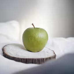 a small green apple sitting on top of a piece of wood