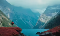 a man is standing on the side of a cliff next to a lake