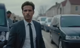 a man wearing a suit walks by a row of parked cars
