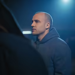a man in a hooded sweatshirt stares ahead at someone else
