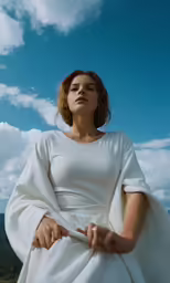 a woman sitting on a ledge outside with a sky background