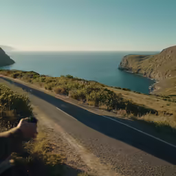 a person holds up a small camera near the road near water