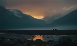 two people in the distance sit under some mountains with sunset