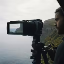 a man holding a video camera near a cliff