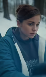 a girl is looking at something while sitting in the snow