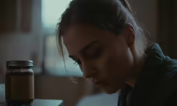 a woman staring down at a jar sitting beside her