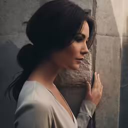 a woman leaning against a wall and looking away