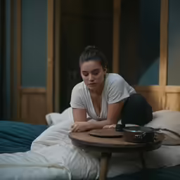 a young woman laying on a bed holding a camera and resting on a stool next to a table