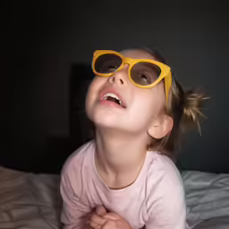 a little girl wearing sun glasses laying on a bed