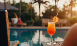 a glass with orange juice sitting by a swimming pool
