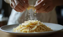 a chef sprinkling cheese onto a white plate