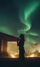 a woman standing in front of an open fire pit looking at the northern lights