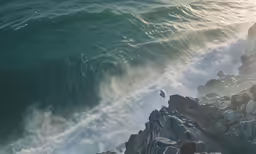 two men watch as a wave crashes near a rocky shoreline