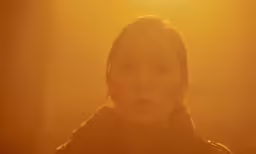 a woman looking into the camera with a sun beam behind her