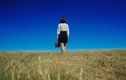 a woman walking through an empty field carrying her suitcase
