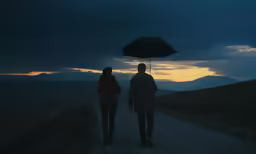 two people walking down a road at night while holding an umbrella