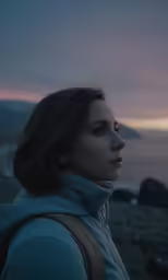 a woman looks to the side at sunset in front of the ocean