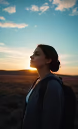 a woman with a backpack stands on a sunset