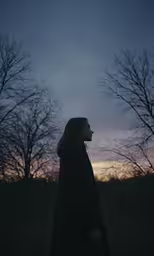 woman in a field at dusk with sky filled with smoke