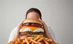a girl hiding her face in front of a hamburger