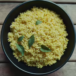 a bowl of yellow rice with a leaf on the side