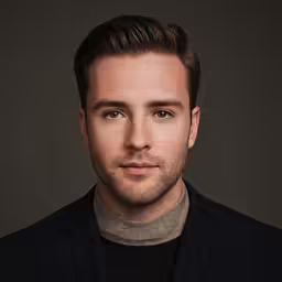 a man with a dark coat and a brown turtle neck sweater is posing for a photograph
