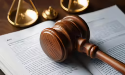 a gavel, book and scales sit on a wooden table