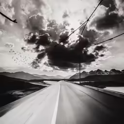 a black and white photo of a highway under cloudy skies