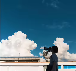 woman standing under cloud holding camera looking at sky