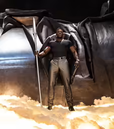 a black man is posing while holding a spear in the sky