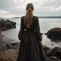 a woman in black dress near water and sky