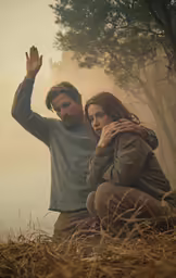 a man and woman sitting on a grass field with their hands up