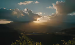 the sun peeking behind some clouds above a valley