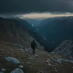 a person walking on a mountain side under a cloudy sky